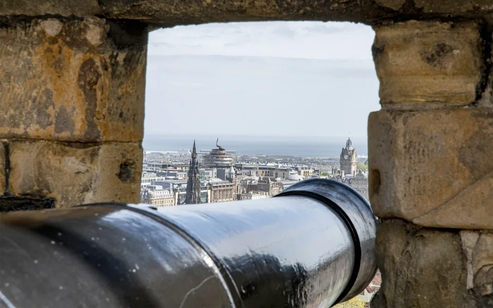 Cannon pointing towards Edinburgh rooftops from a castle embrasure
