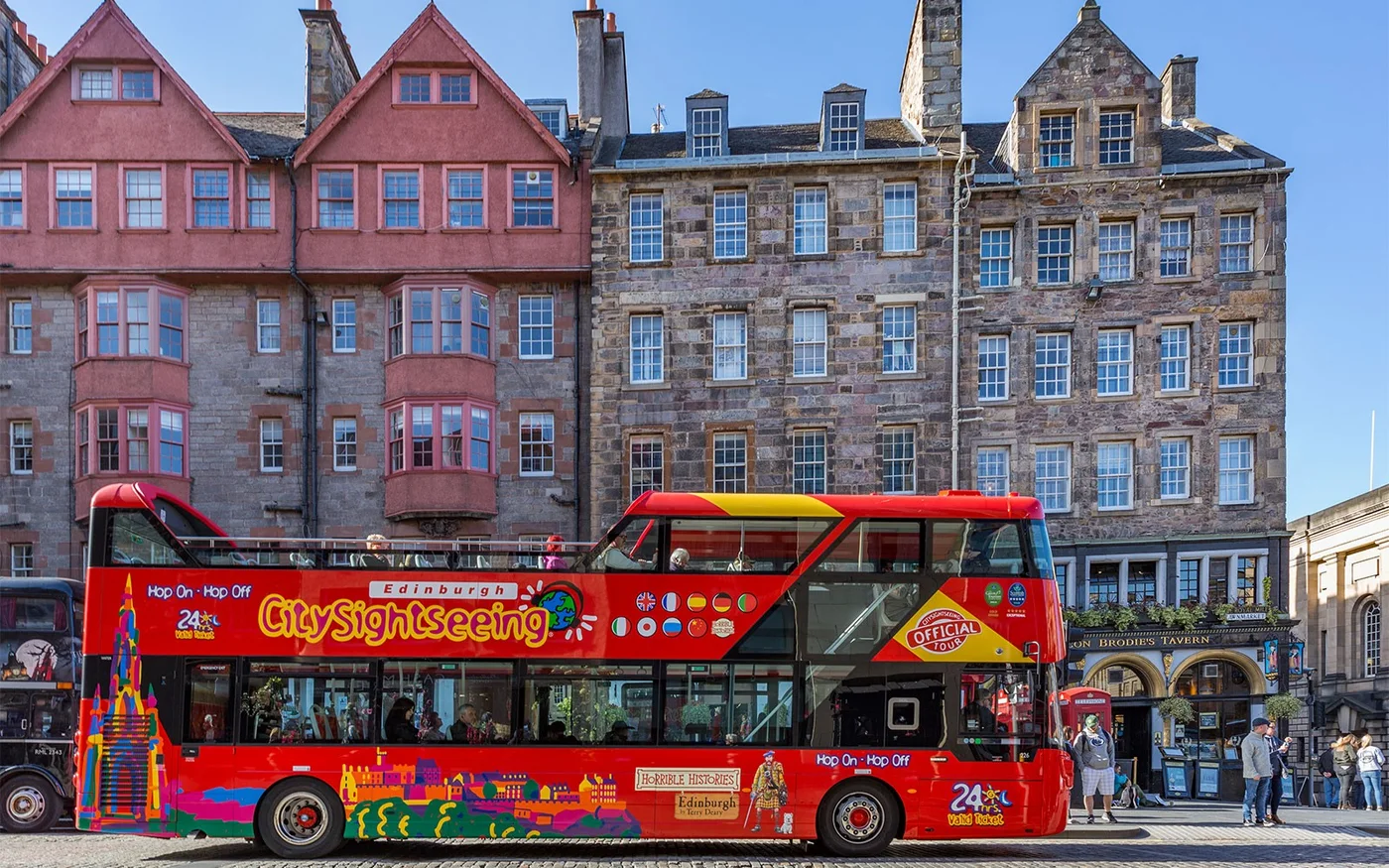 Red sightseeing bus alongside Edinburgh Old Town buildings