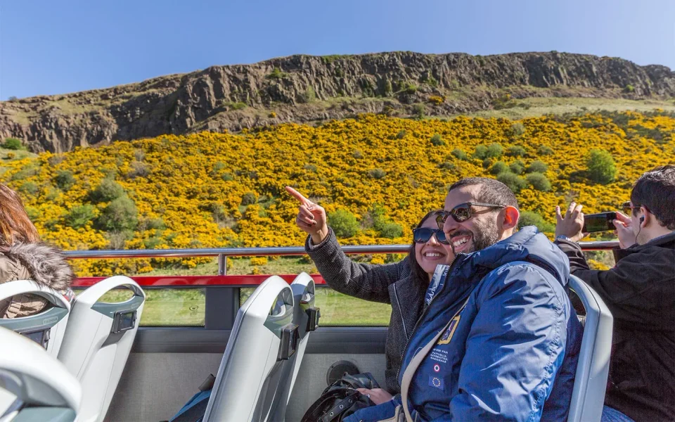 Besucher in einem Open‑Top‑Bus neben einem Hügel