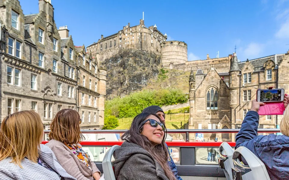 Passengers on an open-top sightseeing bus below the castle