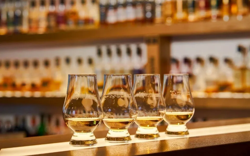 Whisky tasting glasses lined up in front of a bottle collection